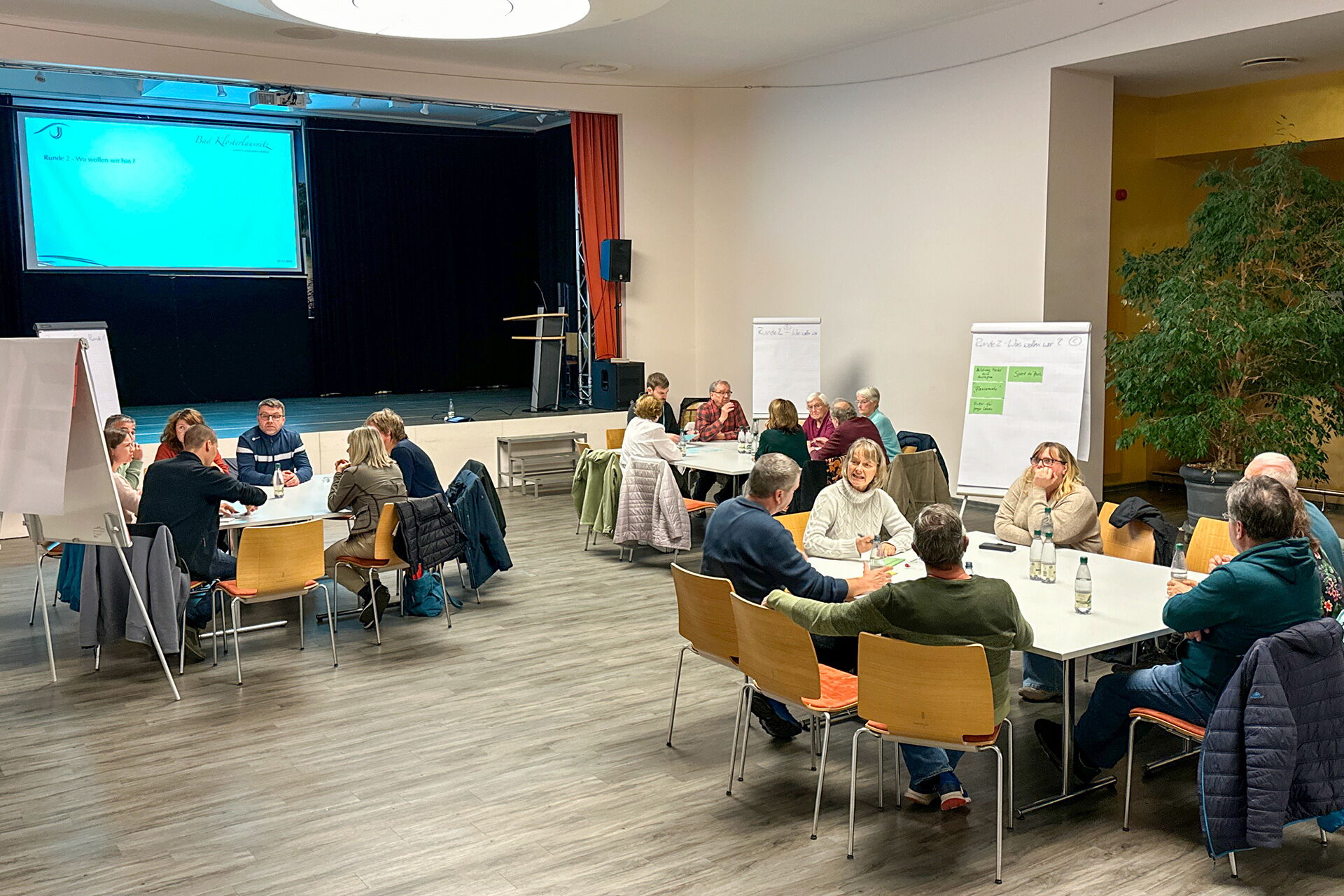 Menschen sitzen in Gruppen an Tischen und diskutieren beim Bürgerdialog am 5.11.2024 im Holzlandsaal