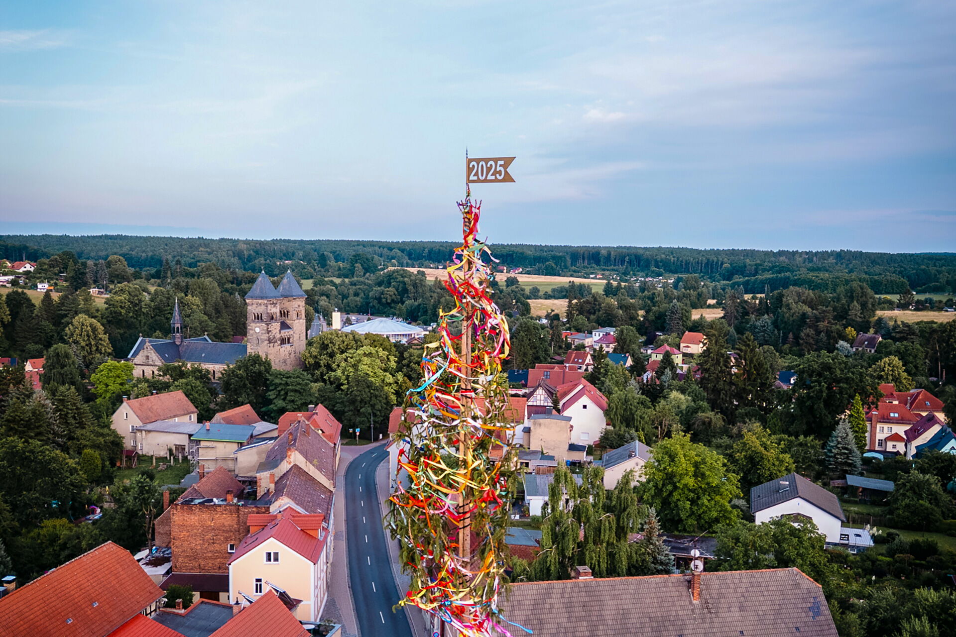 Ein bunt geschmückter Maibaum mit der Jahreszahl 2025 steht im Mittelpunkt eines idyllischen Dorfblicks auf Bad Klosterlausnitz.