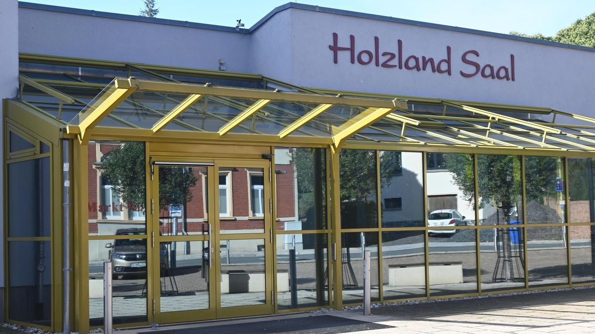 Der Eingang des Holzland Saals zeigt eine moderne Glasfassade mit gelbem Rahmen im Sonnenlicht.