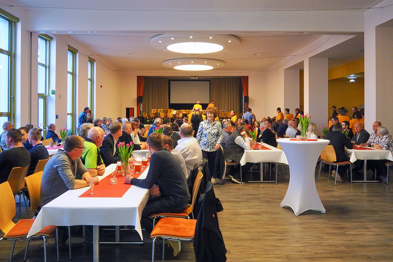 Menschen sitzen zur Firmenfeier an dekorierten Tischen im Holzlandsaal, während eine Frau durch den Raum geht.