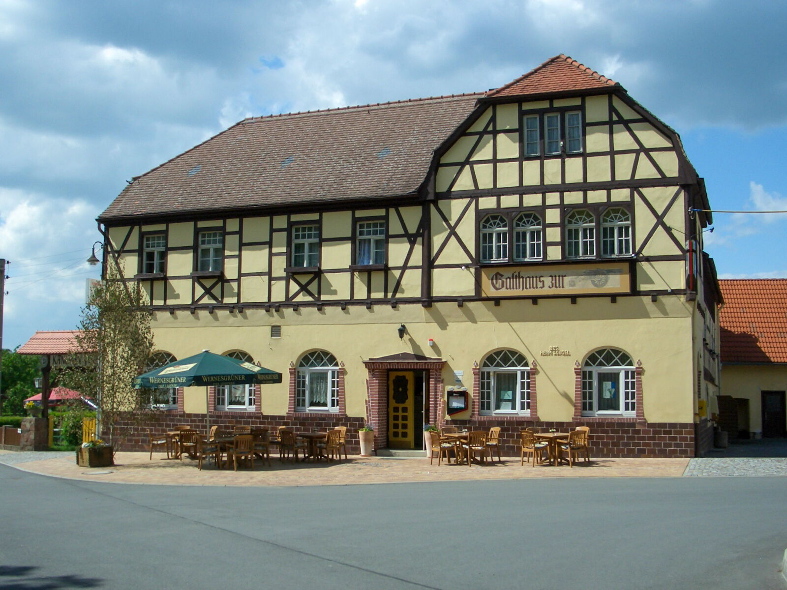 Das traditionelle Fachwerk-Gasthaus „Zur Kanone” mit Terrasse und Sonnenschirmen steht unter einem blauen Himmel.