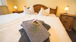 Ein gemütliches Doppelbett mit Holzrahmen im Friedrichshof, dekoriert mit gefalteten Handtüchern und einer kleinen Blume.