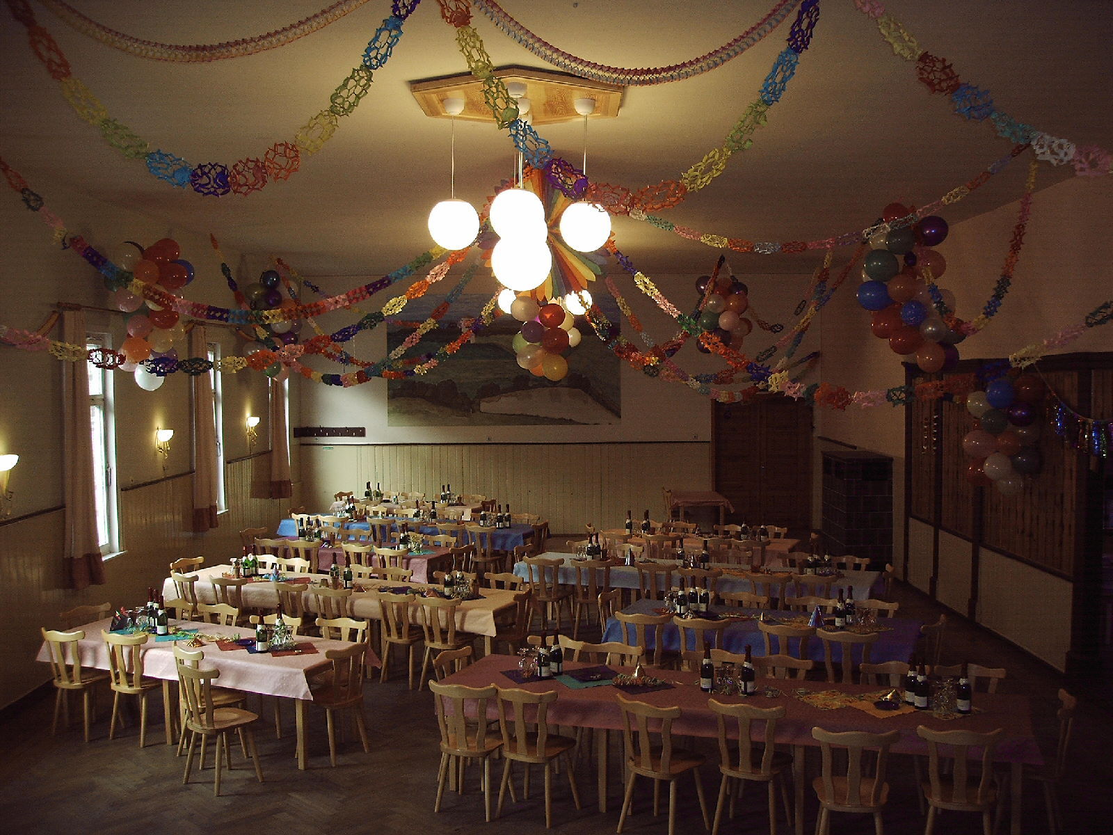 Ein festlich dekorierter Saal mit bunten Girlanden und gedeckten Tischen für eine Feier.