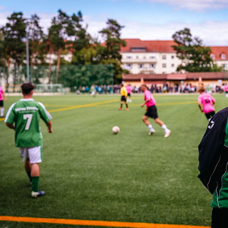 Spieler in grünen Trikots und pinke Gegner kämpfen auf einem Fußballplatz in Bad Klosterlausnitz um den Ball.