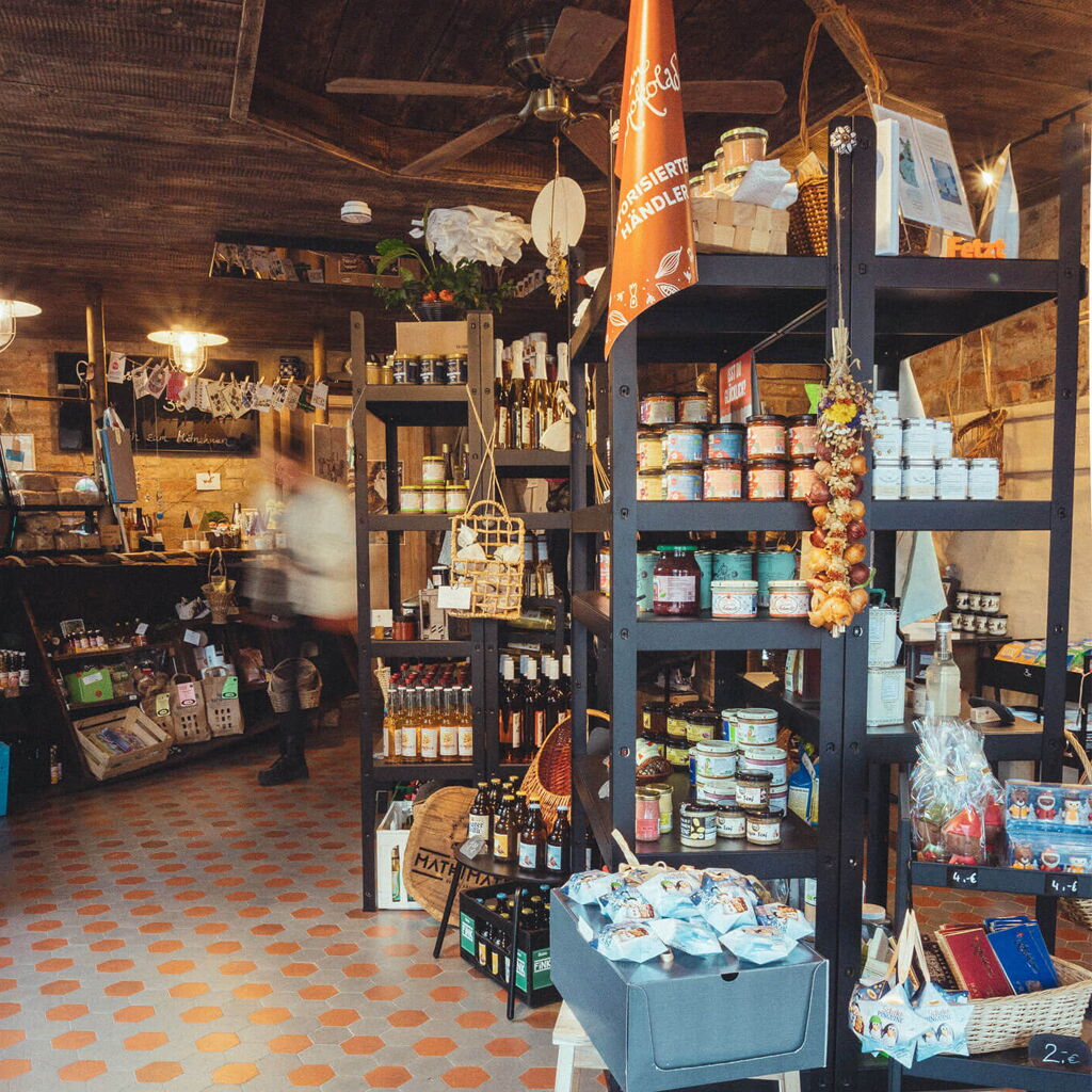 PampelMüse regional.kostbar – Der GenussWarenLaden im Kurort Bad Klosterlausnitz mit Regalen voller Feinkostprodukte und einem Kunden, der durch die Gänge schlendert.