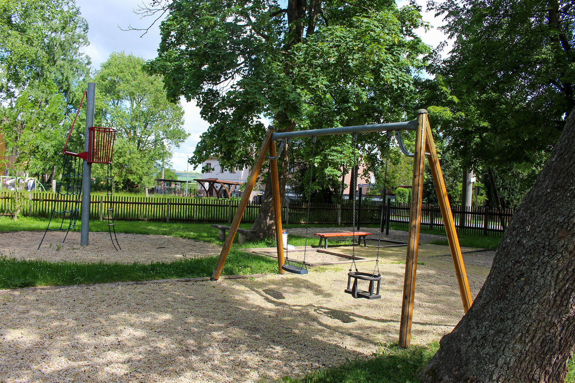 Der Spielplatz im Park von Serba zeigt Schaukeln und Klettergeräte umgeben von grünen Bäumen.
