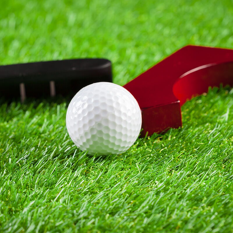 Ein weißer Minigolfball liegt neben Hindernissen auf grünem Kunstrasen, perfekt für ein spannendes Spiel.