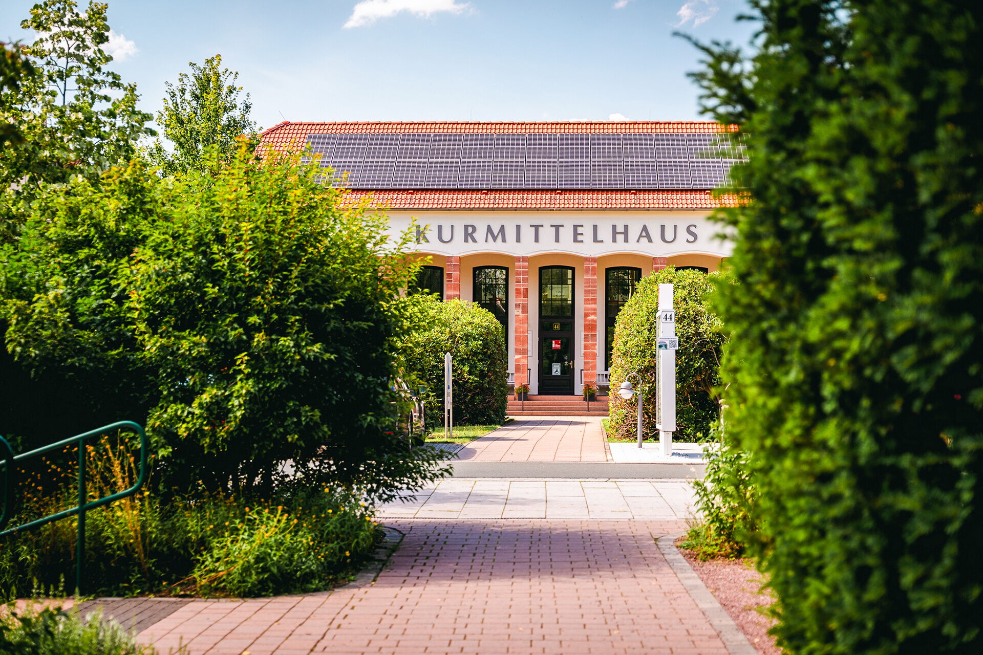 Ein gepflegter Gartenweg führt zum Eingang des Kurmittelhauses, das von üppigem Grün umgeben ist.