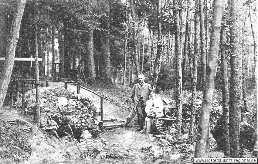 Ein Paar sitzt auf einer Bank neben der historischen Heltzig-Quelle in einem dichten Wald.
