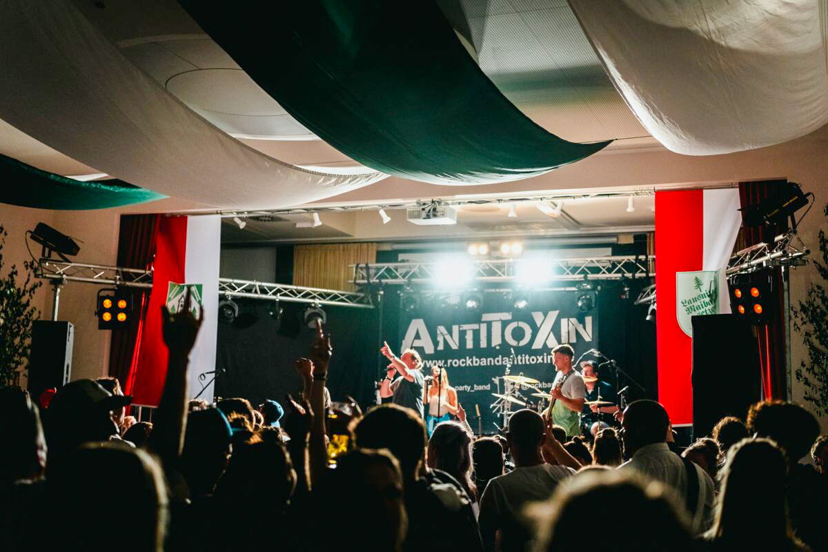 Eine Band spielt energiegeladen auf der Bühne des Holzlandsaals Bad Klosterlausnitz, während das begeisterte Publikum jubelt und feiert.