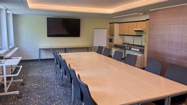 Ein moderner Besprechungsraum mit großem Tisch, Stühlen, TV-Bildschirm und Küchenzeile lädt zu Meetings ein.