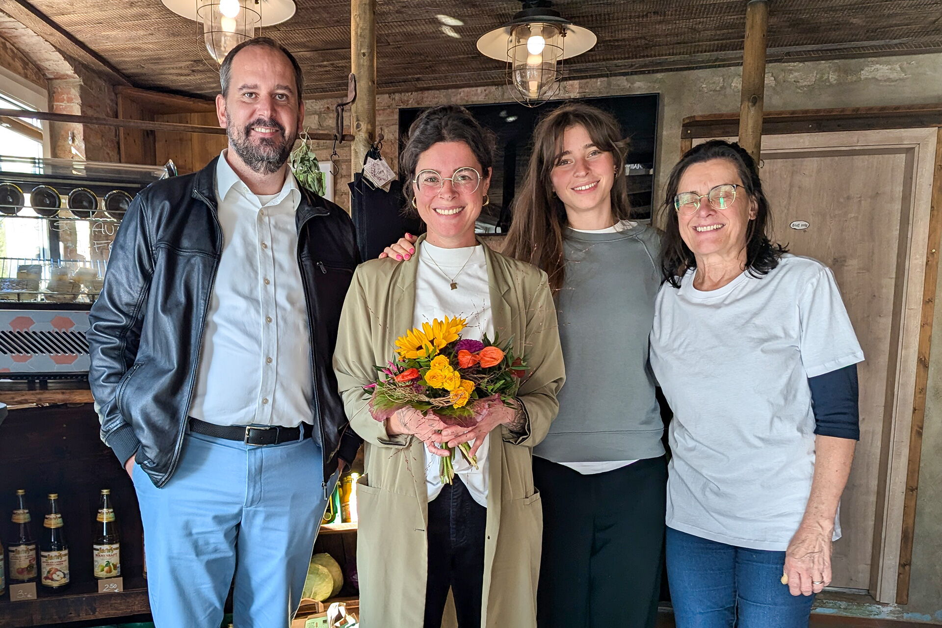 Vier Mitglieder des Pampel Müse Teams posieren lächelnd zusammen in einem gemütlichen Raum, eine Person hält einen Blumenstrauß.