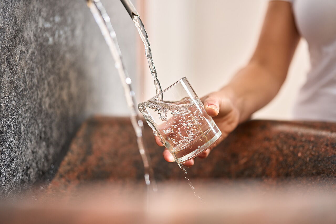 Eine Hand hält ein Glas unter fließendes Wasser aus dem Heilwasserbrunnen im Kurmittelhaus in Bad Klosterlausnitz