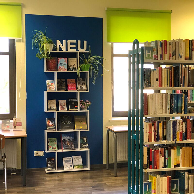Ein Regal mit der Aufschrift "NEU" zeigt Bücher in der hellen Gemeinde- und Kurbibliothek Bad Klosterlausnitz.
