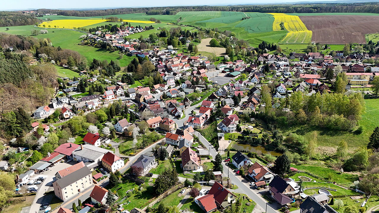 Luftaufnahme von Weißenborn zeigt das malerisches Dorf mit bunten Häusern, umgeben von grünen Feldern und sanften Hügeln.